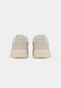 Para beżowo-szarych, codziennych sneakersów widzianych z tyłu, z wytłoczonym napisem "TOMMY JEANS" na koślawo-białych podeszwach.