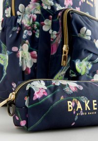 Rucsac floral bleumarin cu fermoare și accente aurii. Include o mică poșetă cu un design similar. Textul include "BAKER" în litere aurii.