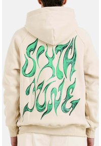 Felpa beige realizzata in tessuto morbido, con una grande stampa grafica verde sul retro che presenta testo stilizzato, e cappuccio con lacci.