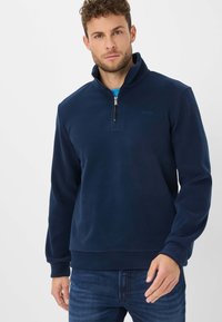 Pullover in pile blu navy con colletto a mezzo zip, maniche lunghe e polsini a costine. Texture liscia, con un logo discreto sul petto.