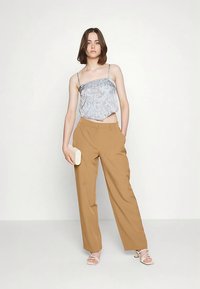 Gaiši zilas rakstainas kamzolītes ar plānām lencītēm kombinācija ar brūnām plašu kāju augstajiem vidukļa biksēm un baltām papēžu sandalēm. Minimālistisks rokassomiņa.