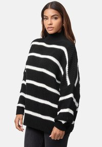 Übergroßer, schwarz-weiß gestreifter Strickpullover mit hohem Kragen und gerippten Bündchen, der eine lockere Passform und eine strukturierte Webart aufweist.