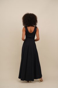 Black maxi dress with a fitted bodice, wide straps, and a V-back. Flared skirt with pleats and smooth texture. Accented with heels.