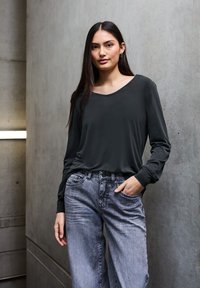 Schwarzes Langarm-Oberteil mit rundem Halsausschnitt, kombiniert mit hellgrauen, weit geschnittenen Jeans. Glattes Material und lockere Passform.