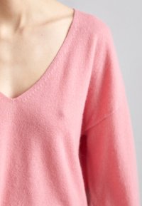 Rosa Wollpullover mit V-Ausschnitt, langen Ärmeln und weicher Textur. Verfügt über einen lässigen Schnitt und minimale Nähdetails.