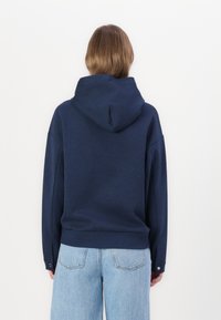 Felpa blu navy con un design ampio, grande cappuccio regolabile e polsini a costine, abbinata a jeans chiari a vita alta.