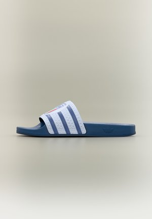 Sandale slide bleue et blanche avec trois bandes bleues et une bride texturée avec un petit logo rond sur un fond neutre.