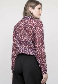 Chemisier à manches longues et transparent, de couleur bourgogne avec un imprimé animalier abstrait blanc. Il dispose d'un col, de poignets à boutons et d'une coupe décontractée.