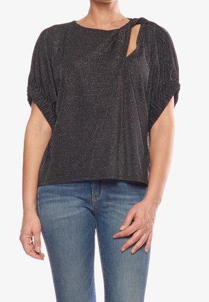 Czarny, teksturowany top z krótkimi bufkami i ozdobnym supłem oraz bocznym wycięciem, wykonany z błyszczącej tkaniny. Noszony z niebieskimi dżinsami.