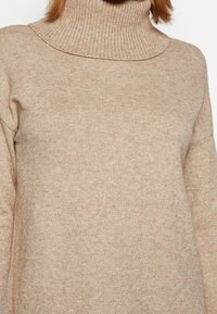 Beżowy sweter z golfem, wykonany z miękkiej, strukturalnej dzianiny. Posiada wysoki, prążkowany kołnierz oraz luźny krój, z opadającymi ramionami dla większego komfortu.