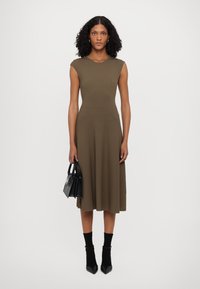 Knit midi dress in olive green, featuring ribbed texture at the bodice. Paired with a black handbag and ankle-length black socks.