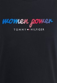 Černé tričko s potiskem "ženská síla" v gradientních barvách: modré, červené a růžové. Název značky "TOMMY HILFIGER" bílou barvou níže.