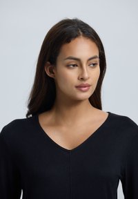 Zwarte, lange mouwen V-hals top; gladde textuur met subtiele naaddetails in het midden; getailleerd ontwerp; zachte stof.