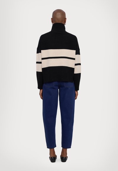 Black and cream striped sweater with a high collar, paired with blue tapered jeans and black flats, viewed from the back.