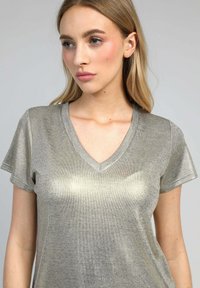 T-shirt V en métal argenté, à manches courtes, texture côtelée, silhouette ajustée, avec un léger éclat et un design simple.