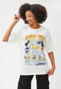 Hvid bomulds t-shirt med farverigt grafisk design med teksten "GROOVY VIBES" samt forskellige illustrerede blomster og svampe. Løs pasform.