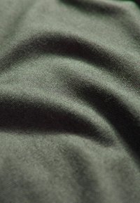 Tessuto verde scuro morbido con trama fine e pieghe delicate che creano ombre e riflessi curvati sulla superficie.