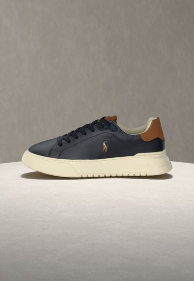 Baskets en cuir bleu marine avec languette de talon marron, semelle épaisse blanche, lacets noirs et petit logo brodé d'un joueur de polo sur le côté.