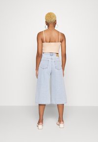 Vista traseira de uma pessoa vestindo uma camisola nua e jeans de cintura alta e pernas largas, de cor azul clara, com uma bainha crua e dois bolsos traseiros.
