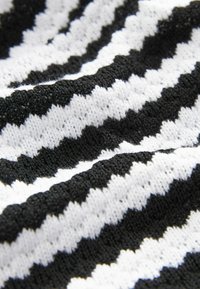 Pletenina v černobílém zigzagovém vzoru, která představuje texturovaný povrch s alternujícími vrcholy a údolími pro zvýšení hloubky.