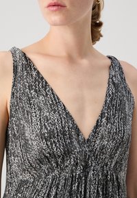Robe à motifs noir et blanc avec un décolleté en V profond, en tissu doux et au design fluide, mettant en avant des motifs circulaires.
