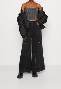 Svart vadderad jacka, grå strapless topp och vida svarta denimbyxor med dragkedjor och fickor. Har kontrasterande sömmar och en lös passform.
