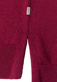 Nahaufnahme eines burgunderfarbenen Strickpullover-Ärmels mit geripptem Bündchen und einem weißen Stoffetikett mit der Aufschrift "MAERZ" an der Naht.