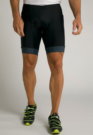 Pantaloni da ciclismo neri con inserto imbottito, caratterizzati da una cinturino e orlo grigi. Indossati con scarpe da corsa nere e verde neon.