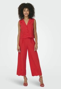 Rode tweedelige outfit met een mouwloze top met perforaties en losse, wijde broekspijpen. Inclusief bijpassende rode sandalen.