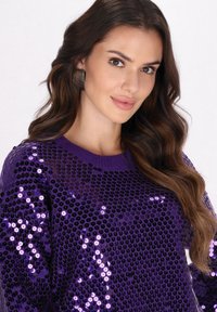 Pulover purpuriu cu paiete, prezentând un decolteu rotund și mâneci lungi, cu o suprafață texturată creată prin suprapunerea paietelor.