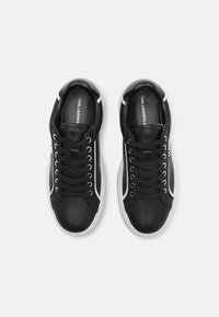 Svarta syntetiska snörskor med vita detaljer, rundad tå, vadderad krage och gummisula. Logotyp synlig på sidan.