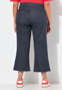Pantalones cortos de mezclilla azul oscuro, con bolsillos traseros y un ajuste relajado, combinados con zapatillas rojas y blancas.