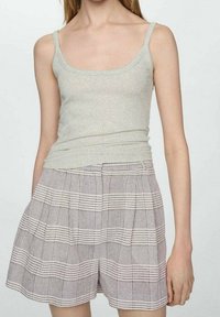 Femme portant un débardeur côtelé sans manches gris clair et un short plissé à carreaux gris taille haute.