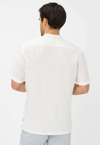 Camicetta bianca in lino a maniche corte con colletto classico e tessuto leggermente strutturato, caratterizzata da un orlo dritto e spacco laterale.