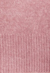 Rosa stickad tyg med en mjuk textur. Har horisontella ribbor i botten. Slät yta med subtila färgvariationer.