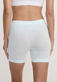 Donna che indossa pantaloni corti fitted senza cuciture di colore blu chiaro e un reggiseno sportivo bianco, mostrata dalla vita in giù su uno sfondo semplice.