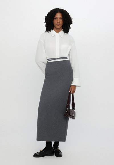 Falda larga gris de tela suave, combinada con una camisa blanca de botones. Los accesorios incluyen un pequeño bolso oscuro y mocasines negros.