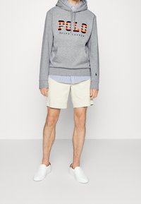 Grå hoodie med "POLO RALPH LAUREN"-logotyp, beiga shorts och vita slip-on-skor. Har en randig skjorta under.