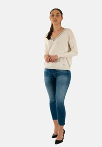 Maglione chiaro in cashmere con scollo a V e bordi grigi a contrasto, abbinato a jeans skinny blu scuro e tacchi alti neri. Tessuto dalla consistenza liscia.