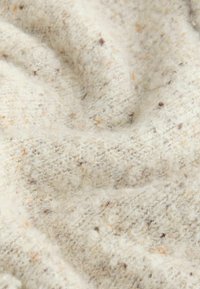 Kareda kreemkangas pruunide ja oranžide laikudega, mis näitab pehmet, karvast pinda ja peent, kootud mustrit.