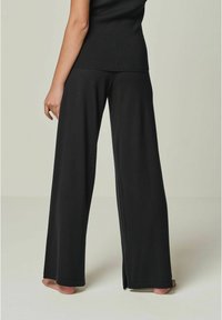 Schwarzweite Hosen aus weichem Stoff mit hoher Taille, seitlichen Schlitzen und glatter Textur. Die Rückansicht zeigt eine lockere Passform.