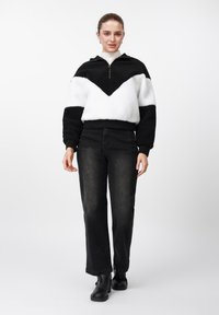 Mustvalge värvilahendusega fliisist dressipluus V-kujulise mustriga, kokku sobitatud kõrge vöökohaga mustade teksade ja mustade pahkluusaabastega.