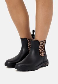 Botas negras de goma hasta el tobillo con un panel lateral elástico de estampado de leopardo, suela texturada y tira en la parte superior para ponerlas con facilidad. Acabado suave y diseño duradero.
