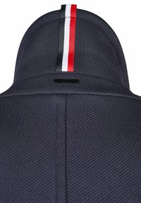 Navyblaues strukturiertes Gewebe mit einem hohen Kragen. Verfügt über einen zentralen vertikalen Streifen in Rot, Weiß und Schwarz. Enthält ein kleines schwarzes Logoetikett.