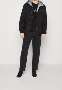 Svart lättviktsjacka med grå foder, dragkedjestängning, elastiska manschetter, ihopparad med en svart t-shirt och mörka jeans, samt svarta sneakers.