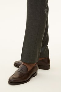 Braune Leder-Löcher mit einem gesteppten Mokassin-Zehen-Design, kombiniert mit strukturierten braunen Socken und dunkelgrauen maßgeschneiderten Hosen.