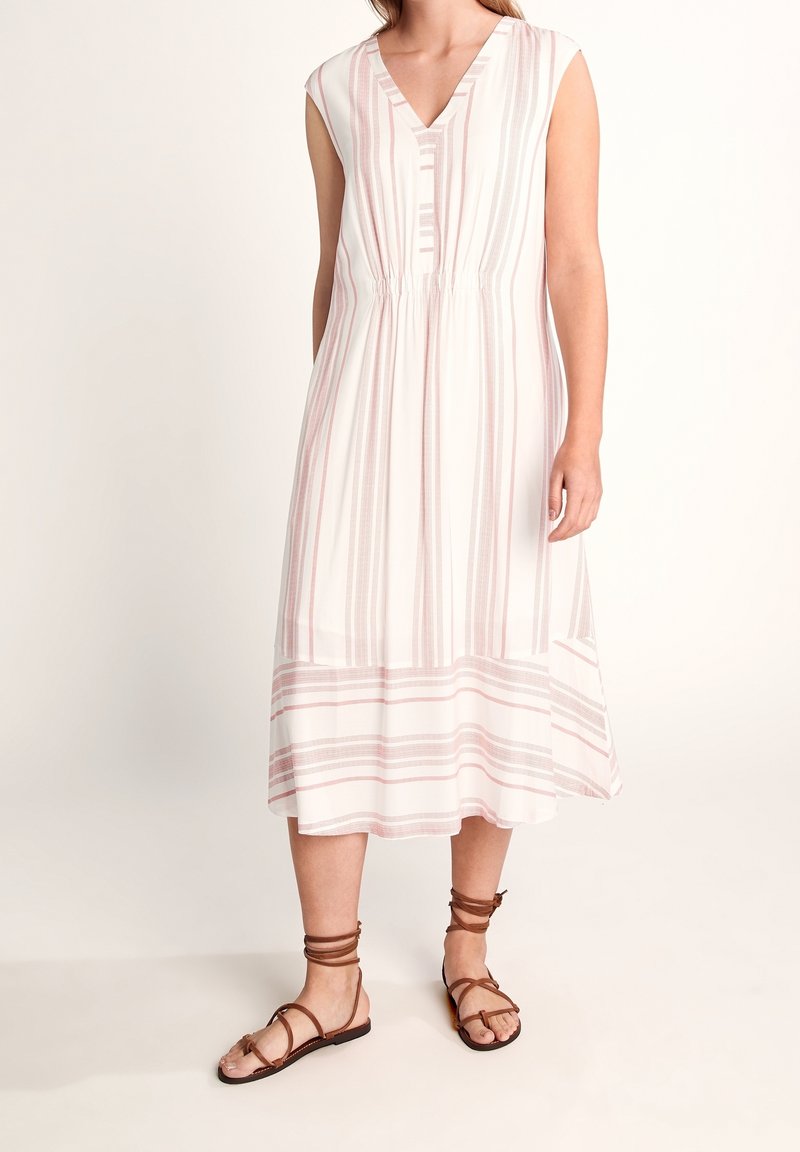 Femme portant une robe midi blanche sans manches avec des rayures verticales et horizontales roses, associée à des sandales marron en cuir avec un lien à la cheville.