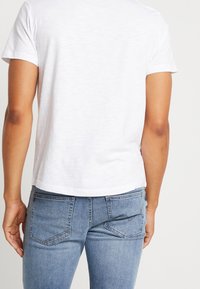 Camiseta blanca de manga corta hecha de tela suave, con un corte holgado. Combinada con unos vaqueros de denim azul claro que tienen dos bolsillos traseros.