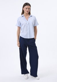 Camicia a maniche corte a righe blu chiaro e bianche con colletto, abbinata a pantaloni a gamba larga blu navy e sneakers bianche. Design semplice e casual.