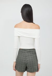 Biała bluzka odsłaniająca ramiona z długimi rękawami w połączeniu z szarymi spodniami w kratę o dopasowanym kroju i fakturowanej tkaninie.